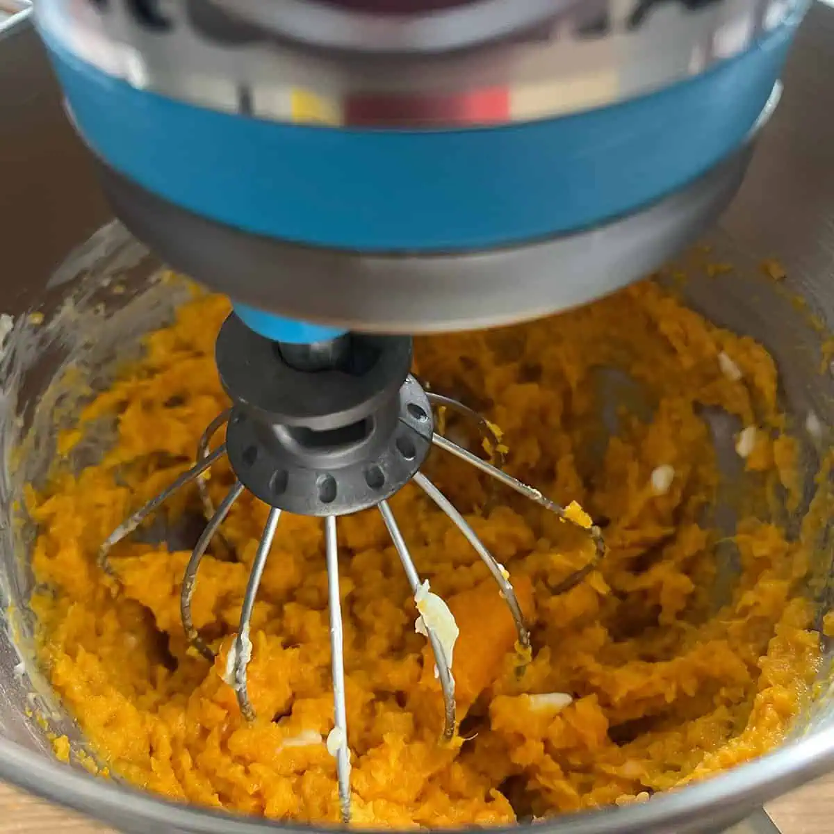 Stand mixer whisk mixing roasted sweet potatoes with softened butter in a metal bowl.