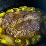 Slow cooker Mississippi pot roast in broth with pepperoncini peppers and sliced onions before shredding