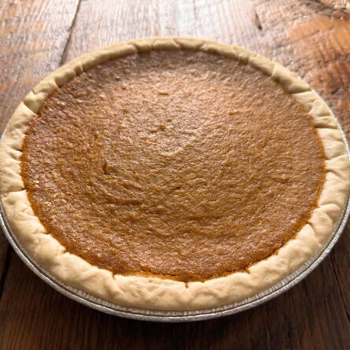 Homemade sweet potato pie in a foil pie tin on a rustic wooden surface.
