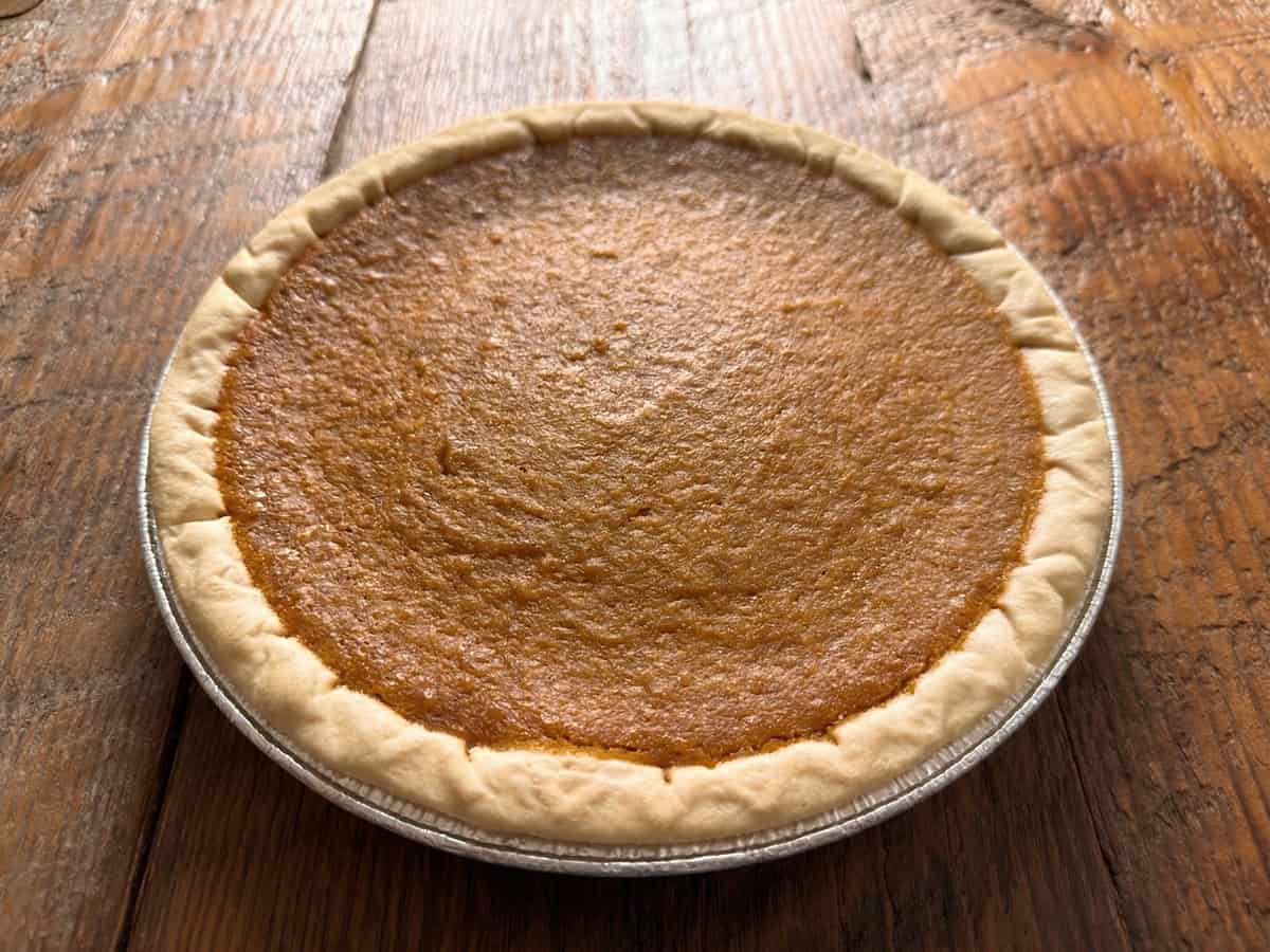 Homemade sweet potato pie in a foil pie tin on a rustic wooden surface.