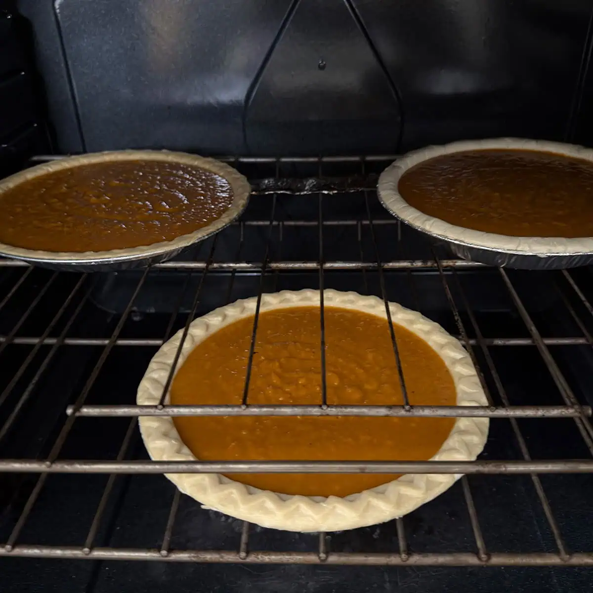 Three sweet potato pies baking in the oven on staggered racks.