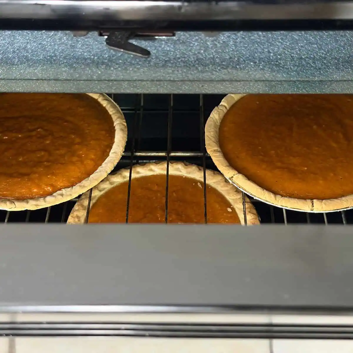 Three baked sweet potato pies cooling in the oven with the door slightly open.