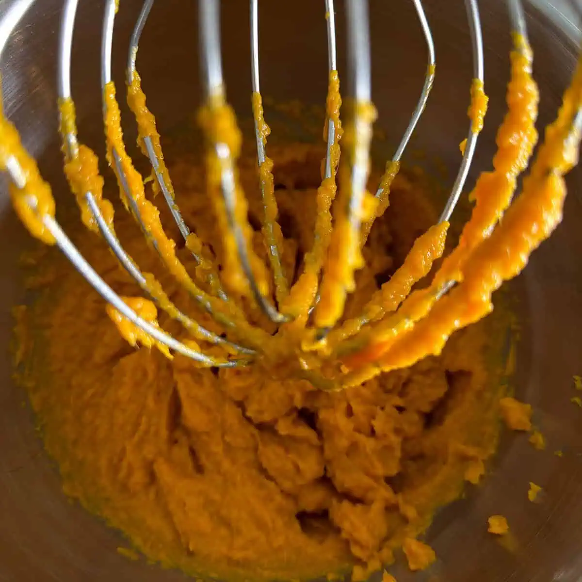 Stand mixer whisk attachment with stringy sweet potato puree clinging to the wires.