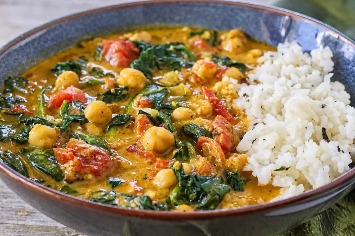 Close-up of creamy chickpea curry with spinach and tomatoes served with rice.