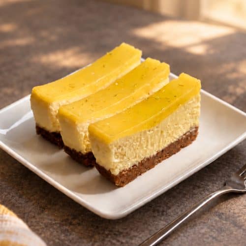Three gluten-free key lime bars with creamy filling, a graham-style crust, and glossy lime topping on a white plate.