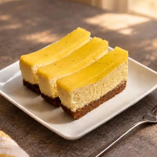 Three gluten-free key lime bars with creamy filling, a graham-style crust, and glossy lime topping on a white plate.