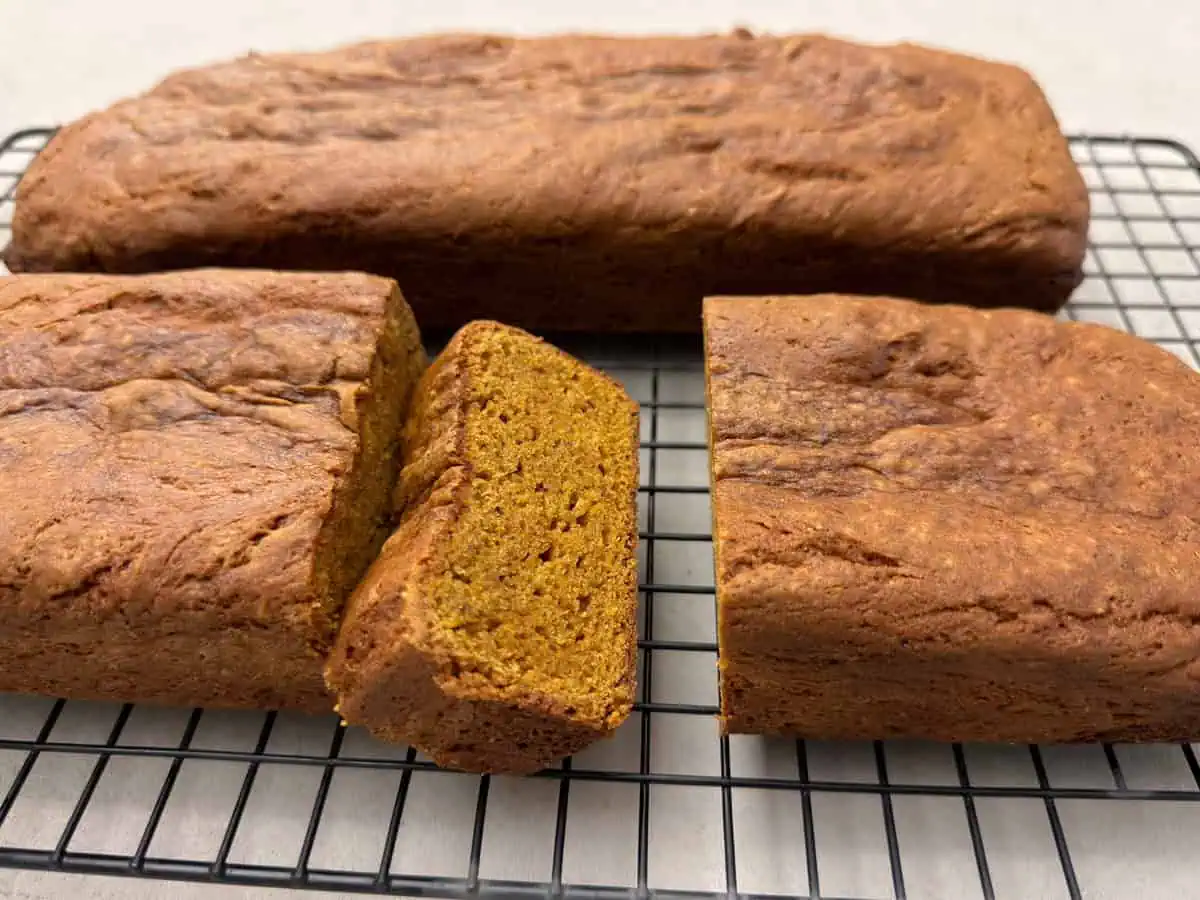 Sliced gluten-free pumpkin bread with a moist orange-brown crumb, served on a cooling rack beside the remaining loaf.