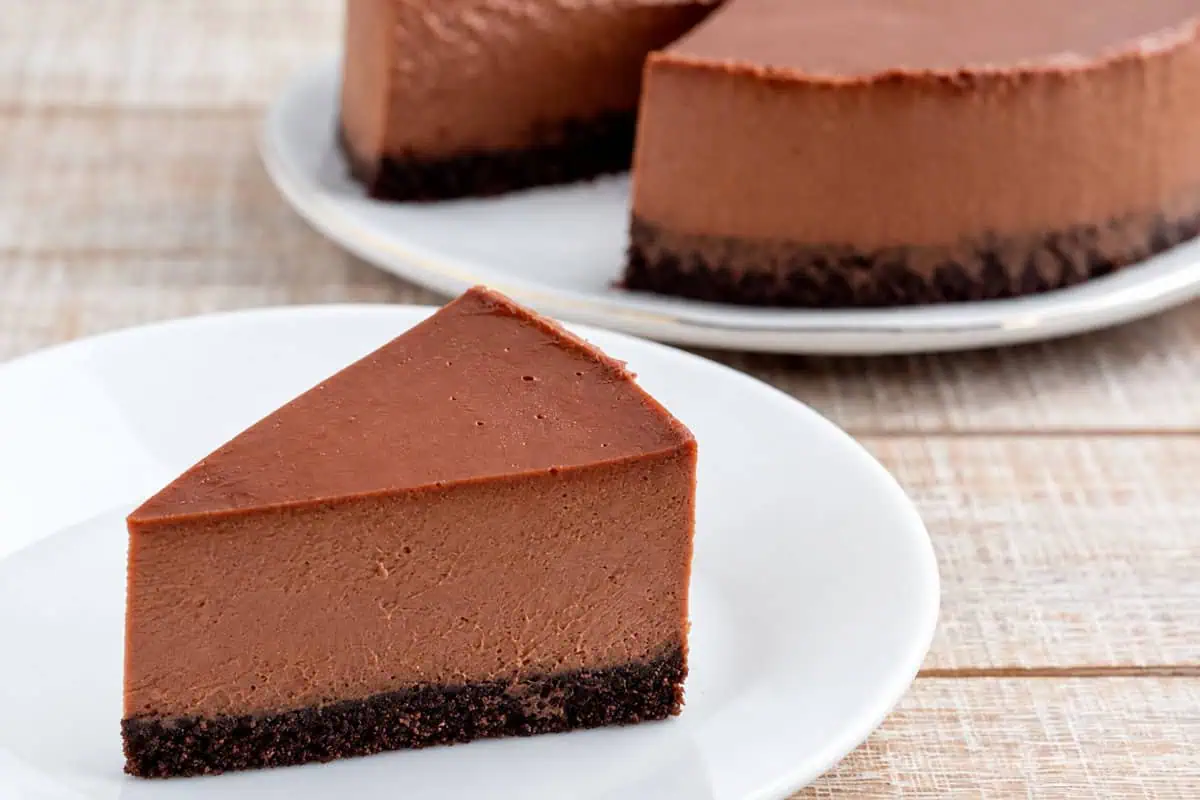 Slice of chocolate cheesecake on a white plate, with the remaining cake behind it.
