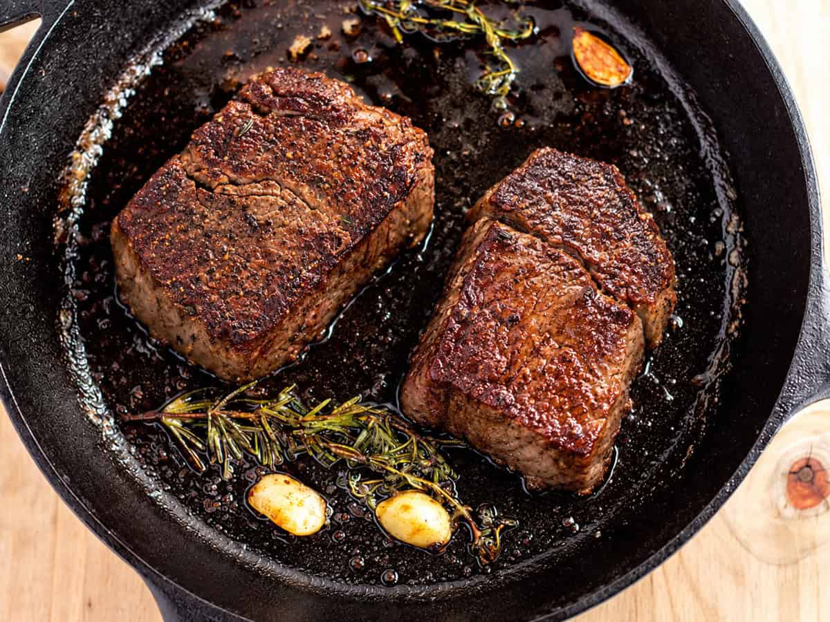 Two filet mignon steaks seared in a cast iron skillet with garlic and herbs