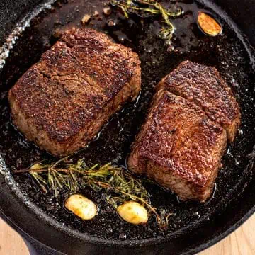 Two filet mignon steaks seared in a cast iron skillet with garlic and herbs