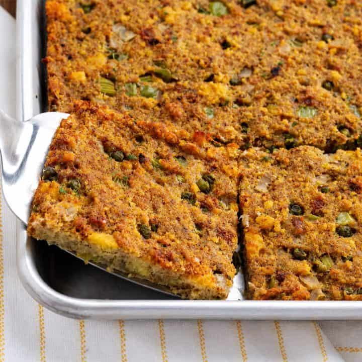 Southern cornbread dressing with browned crisp edges lifted from a sheet pan on a serving spatula