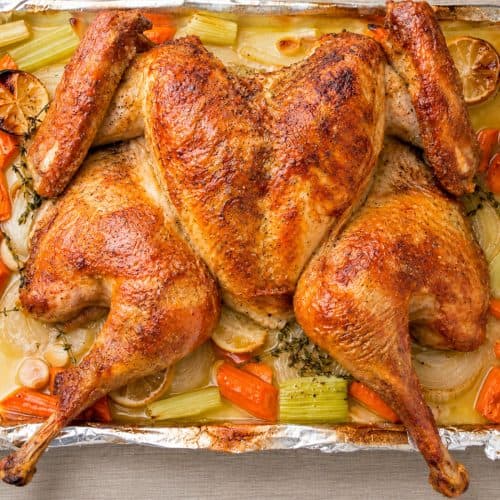 Spatchcock turkey roasted flat on a sheet pan with crisp browned skin and vegetables around it