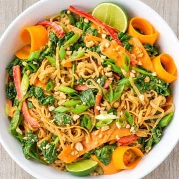 Thai noodle salad topped with peanuts and green onions, with lime wedges.